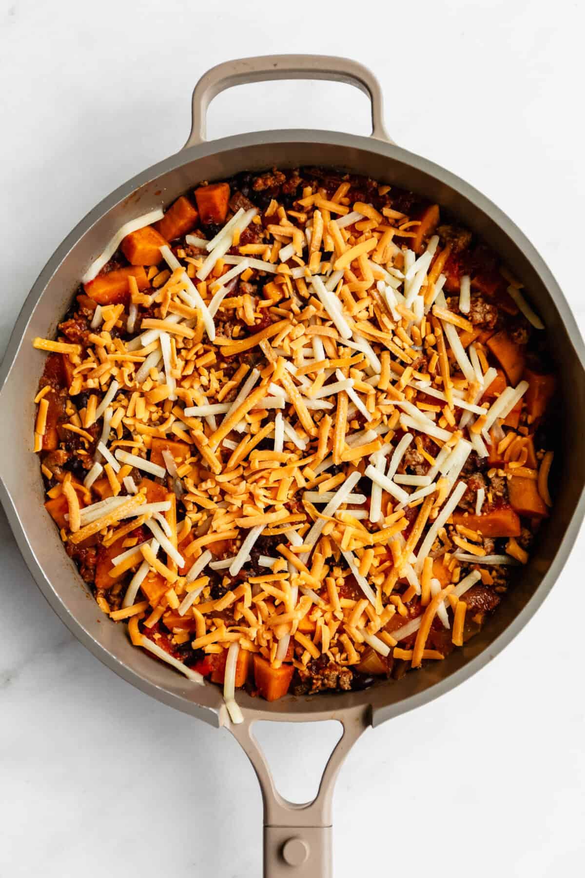 shredded cheese on top of ground turkey and sweet potato in a pan.