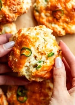 two hands breaking a jalapeno cheddar cottage cheese biscuit in half.