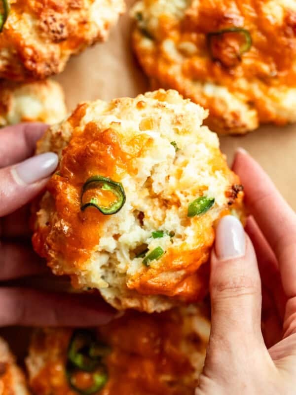 two hands breaking a jalapeno cheddar cottage cheese biscuit in half.