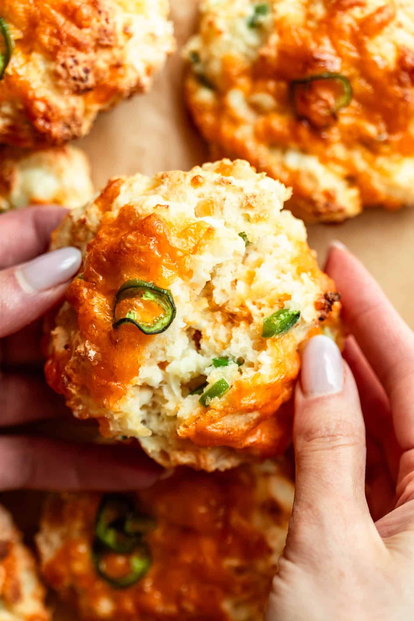 two hands breaking a jalapeno cheddar cottage cheese biscuit in half.