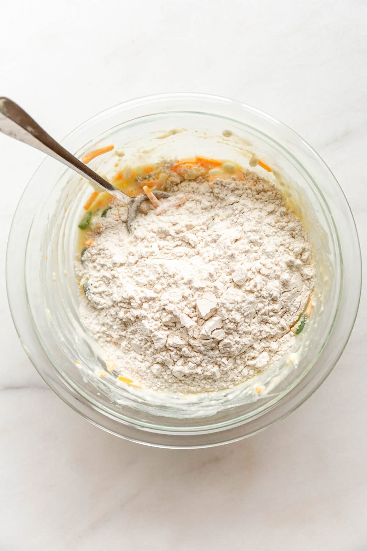 A glass bowl with flour added to the cheddar jalapeño cottage cheese biscuit mixture.