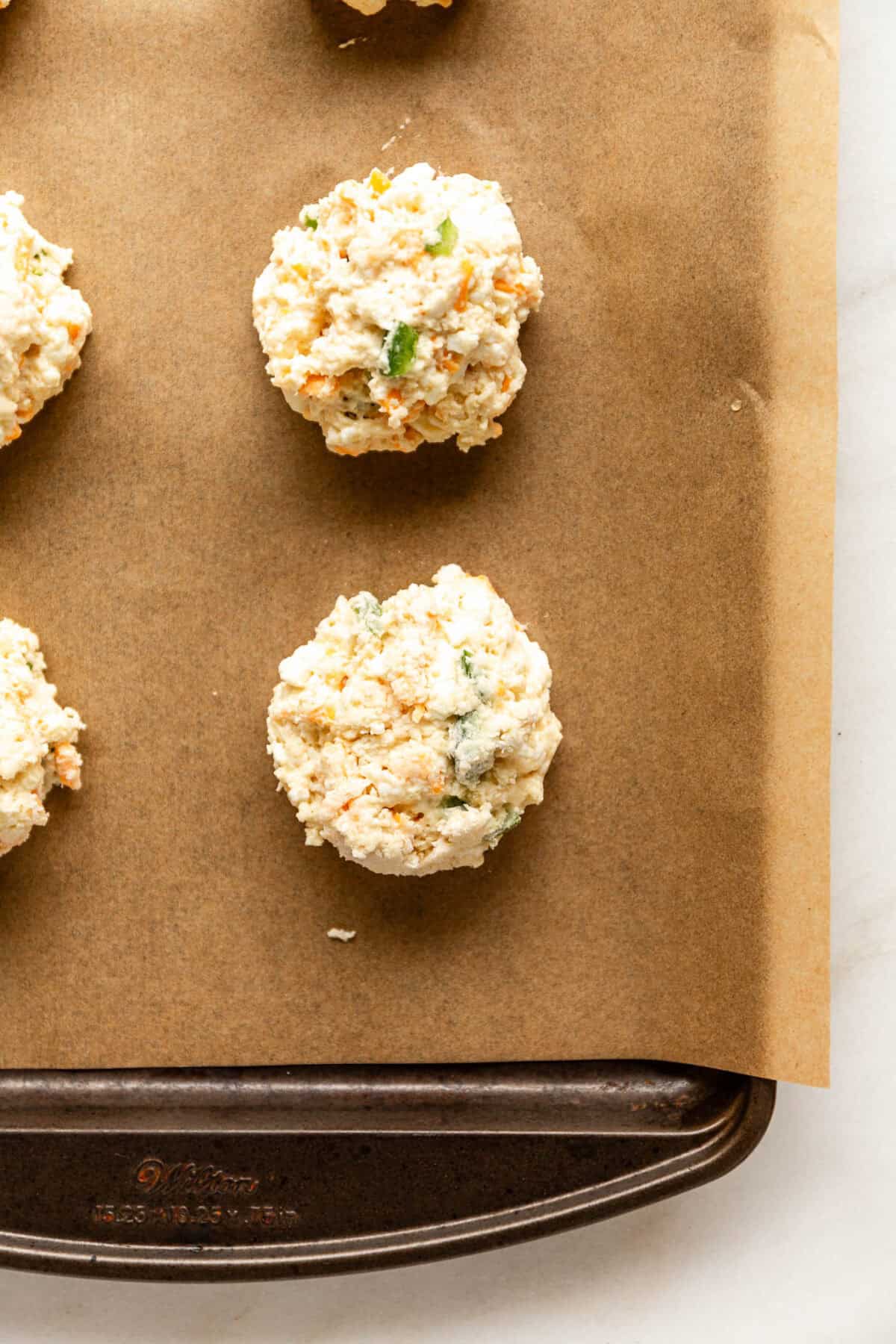 Unbaked cheddar jalapeño cottage cheese biscuit dough balls on a parchment-lined baking sheet.