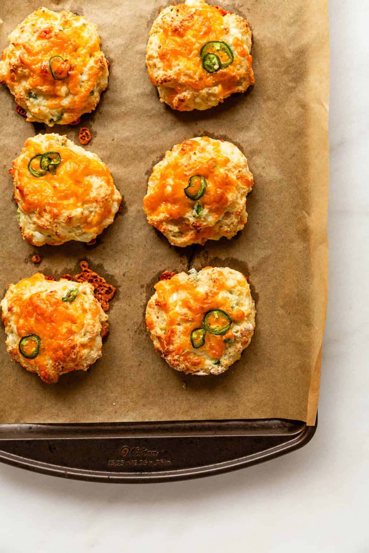 Close-up of golden baked cheddar jalapeño cottage cheese biscuits topped with sliced jalapeños on parchment paper.