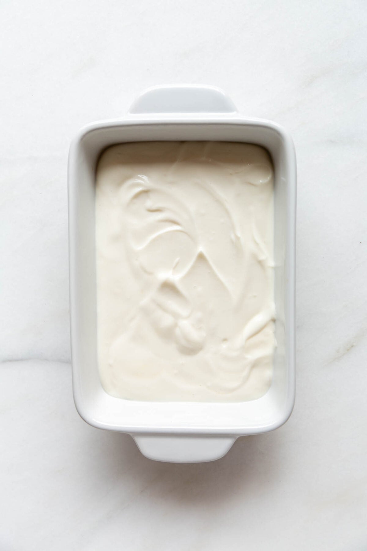 A white rectangular baking dish with cream layer for Greek yogurt tiramisu