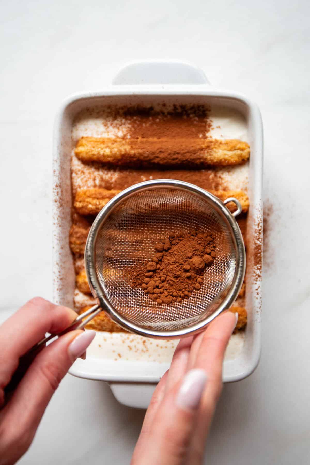 A baking dish showing assembled layers of soaked ladyfingers and cocoa for Greek yogurt tiramisu