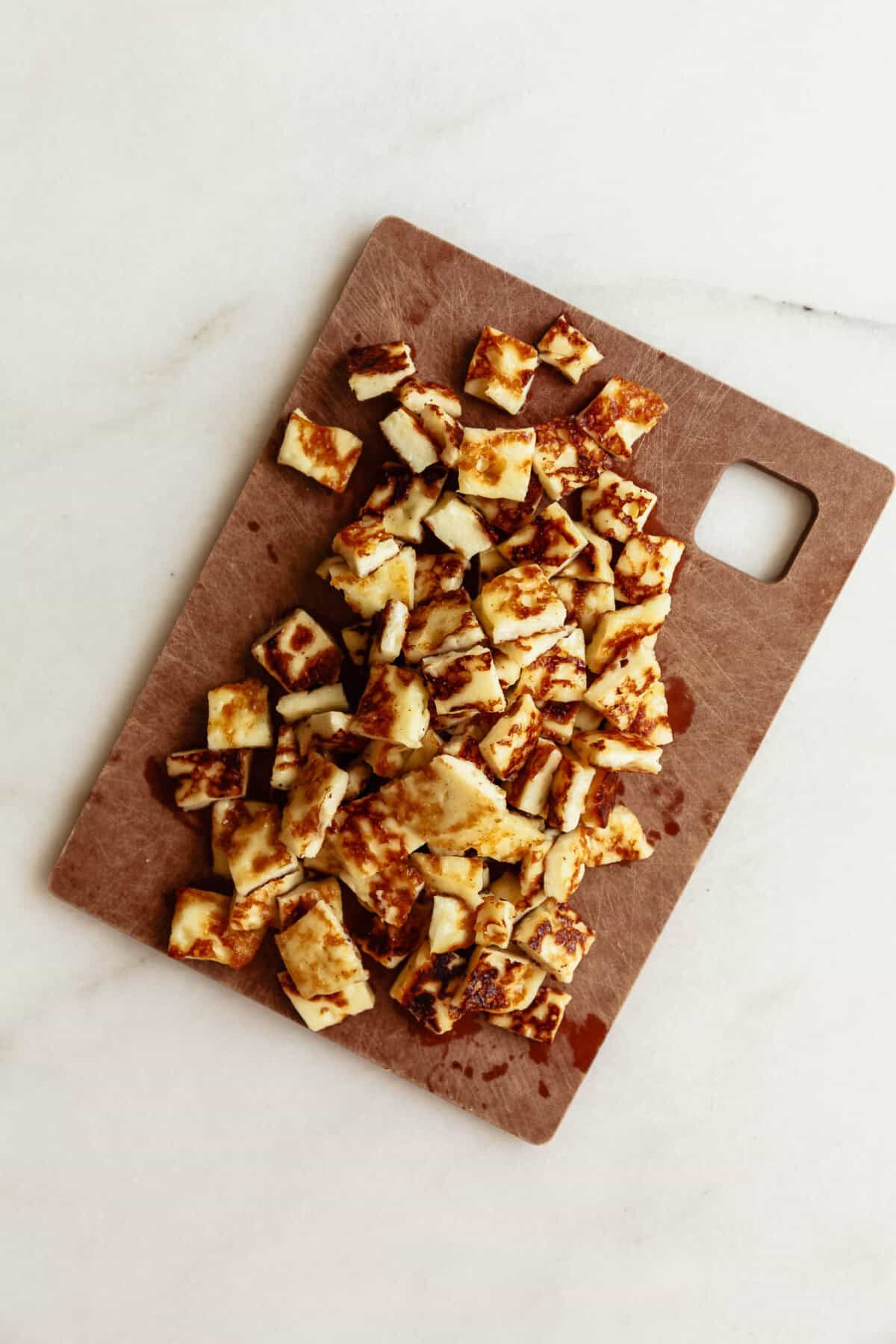 chopped pan-fried halloumi on a brown cutting board.