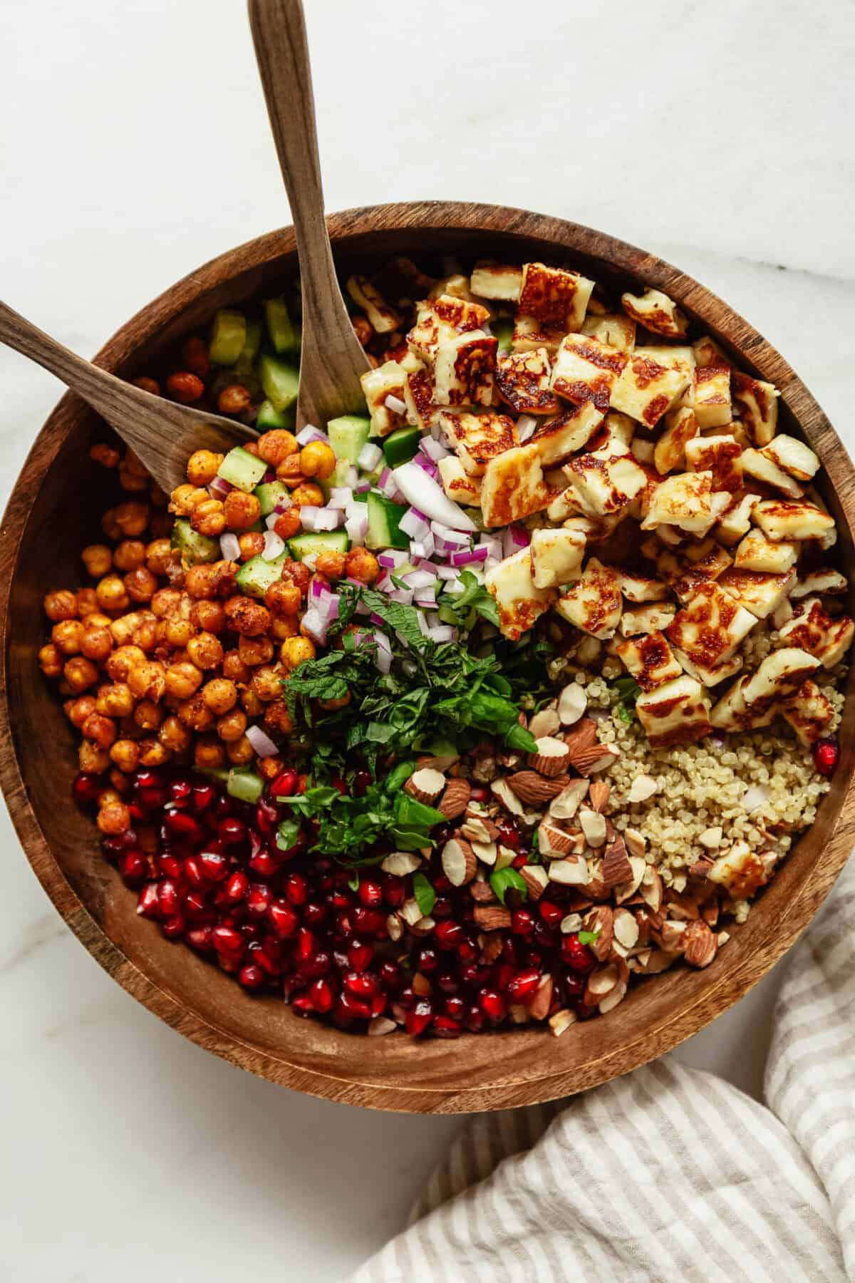 a roasted chickpea halloumi salad in a wood bowl with two wooden spoons.