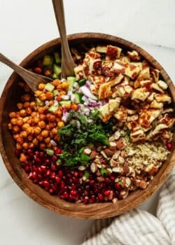 a roasted chickpea halloumi salad in a wood bowl with two wooden spoons.
