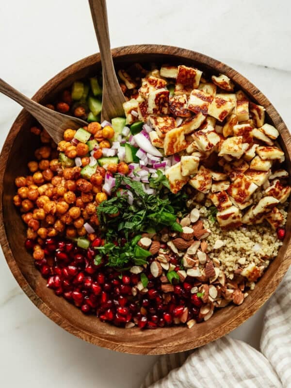 a roasted chickpea halloumi salad in a wood bowl with two wooden spoons.