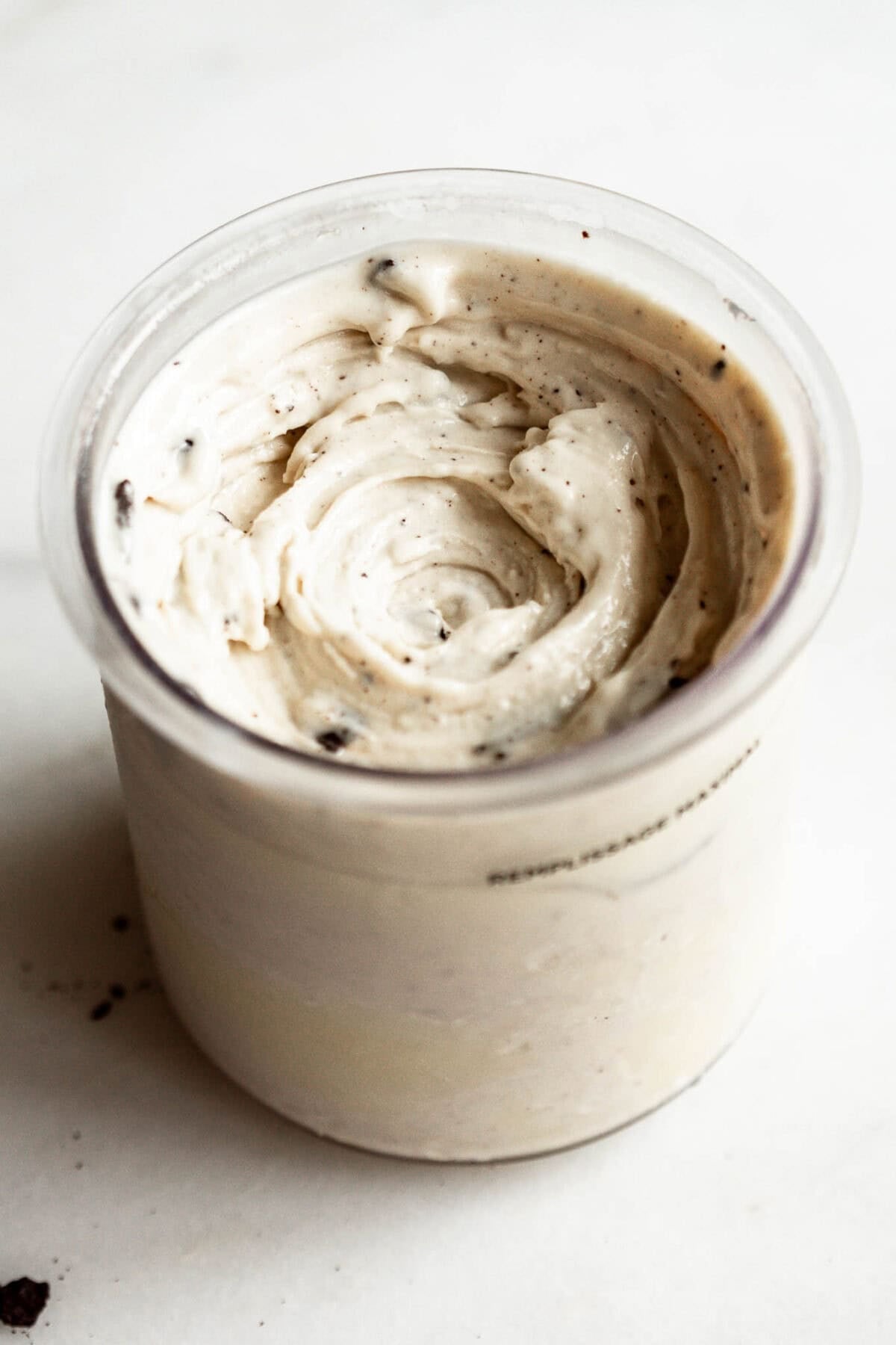 Ninja Creami container filled with finished cookies and cream ice cream, showing swirled creamy texture with Oreo cookie bits mixed throughout.