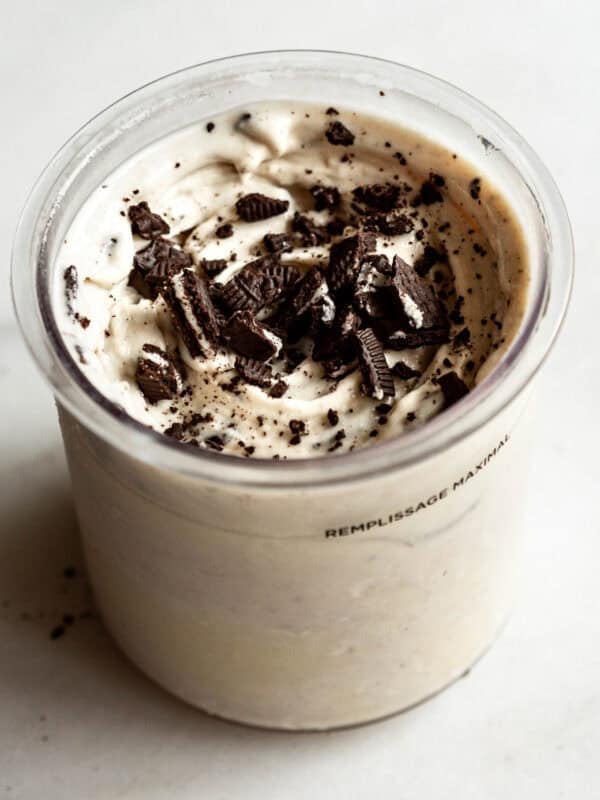 Cookies and cream Ninja Creami in a container topped with crushed Oreo cookies and chocolate cookie pieces.