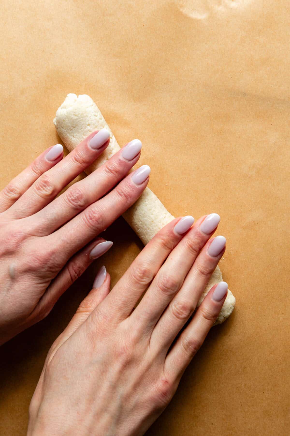 two hands rolling out bagel dough.