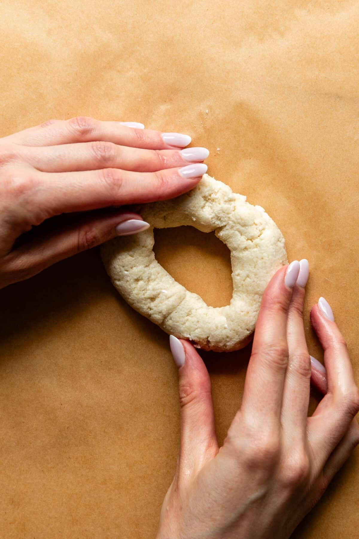 two hands shaping dough into a bagel.