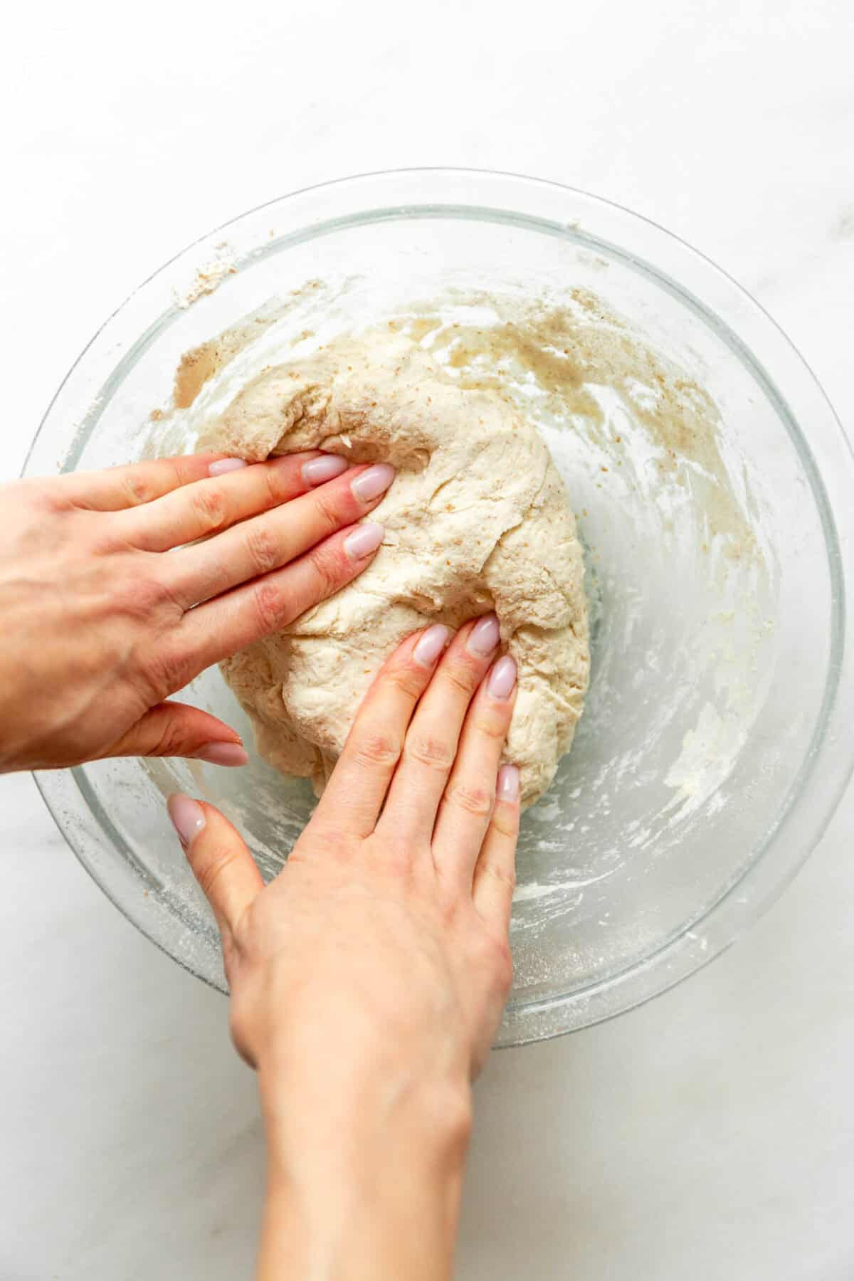 Hands kneading cottage cheese cinnamon roll dough in a glass bowl.