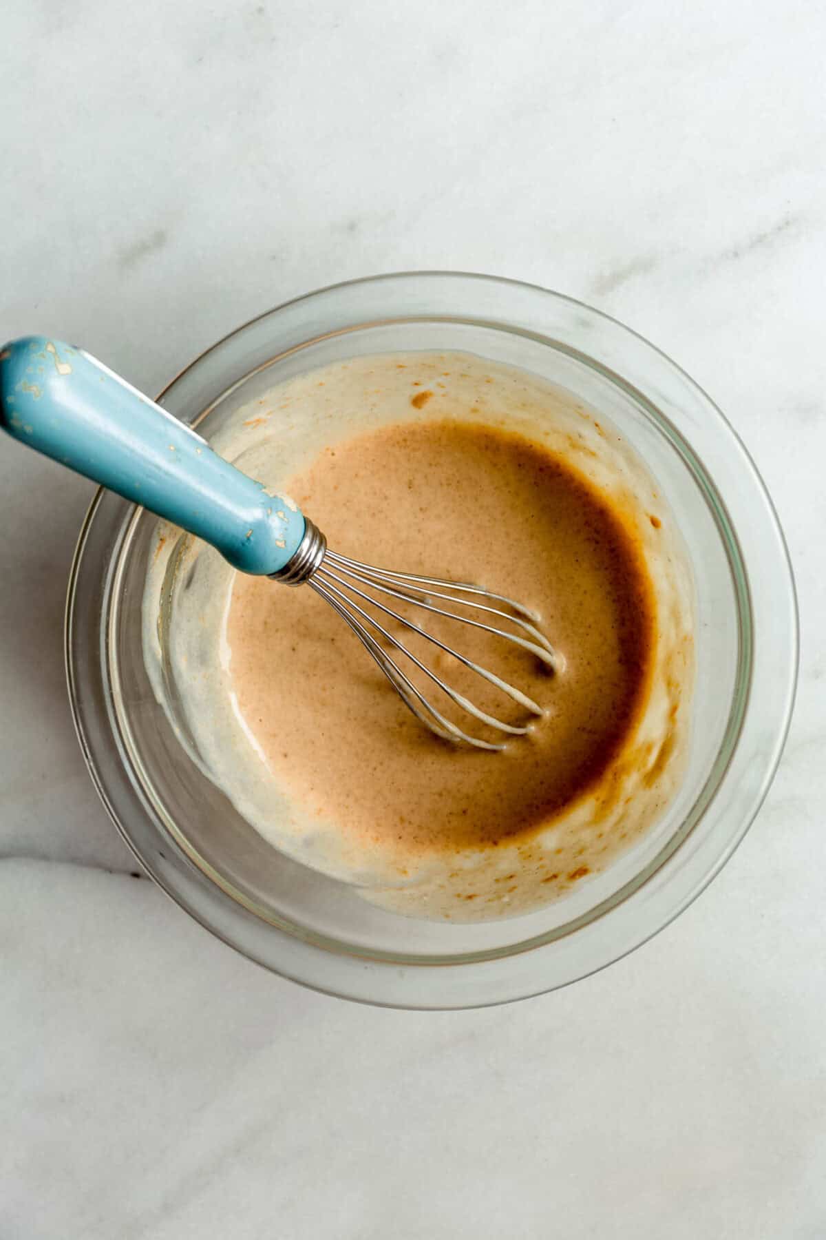 blended cottage cheese with nut butter maple syrup and vanilla in a clear bowl with a blue whisk.