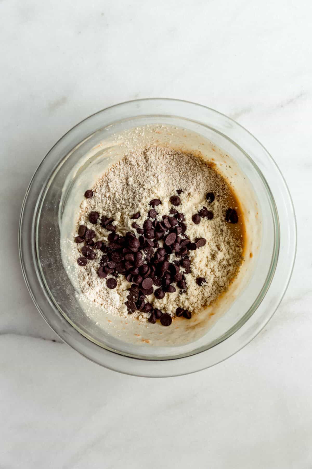 Oat flour, chocolate chips and cottage cheese mixture in a clear mixing bowl.