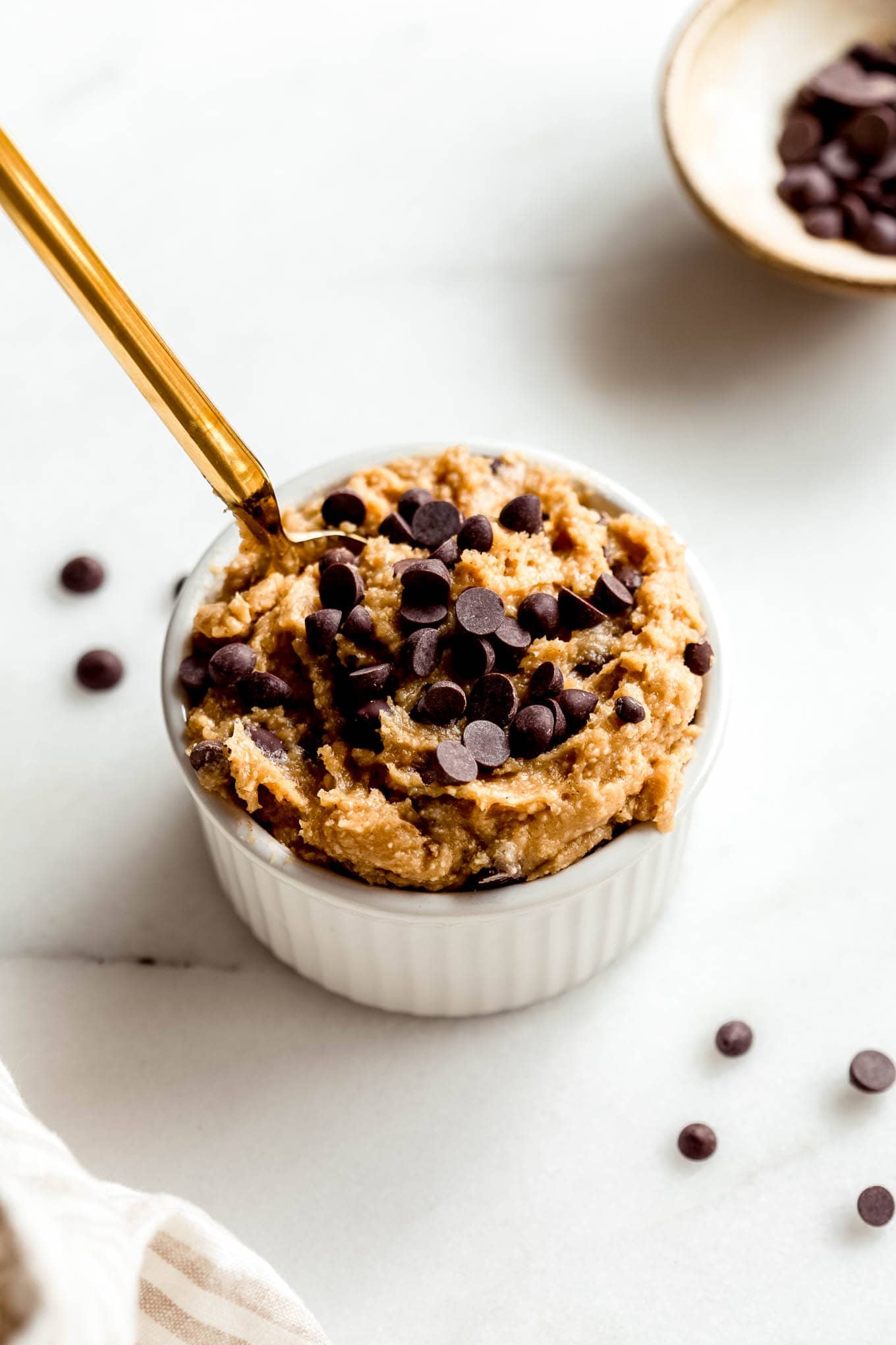 Cottage cheese cookie dough in a white ramekin with a small bowl of chocolate chips on the side.