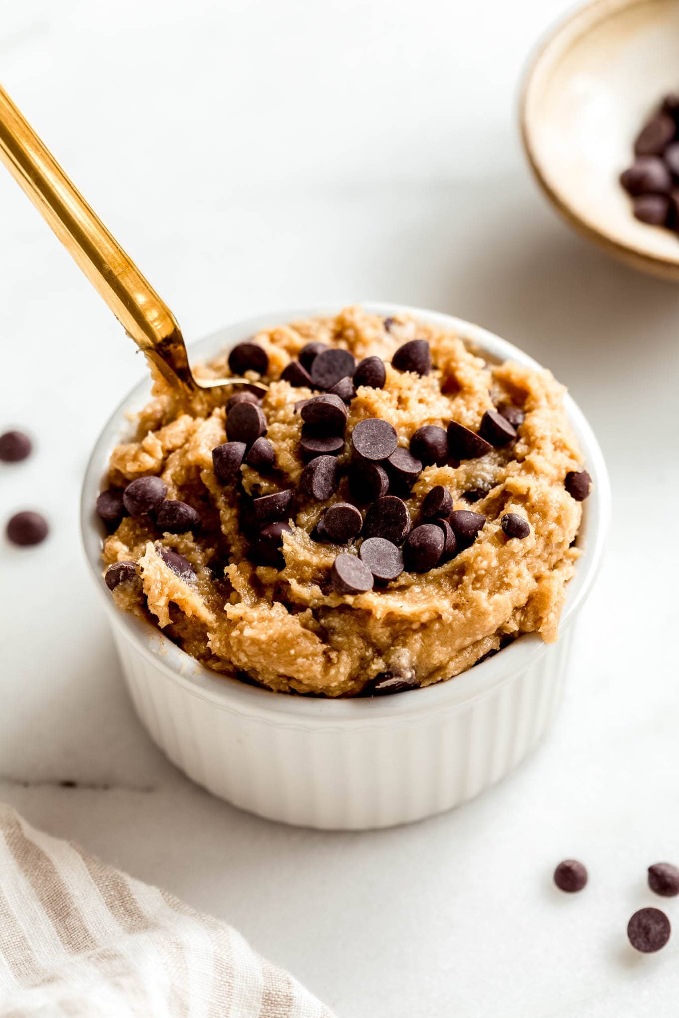 Cottage cheese cookie dough in a white ramekin with a gold spoon in it.