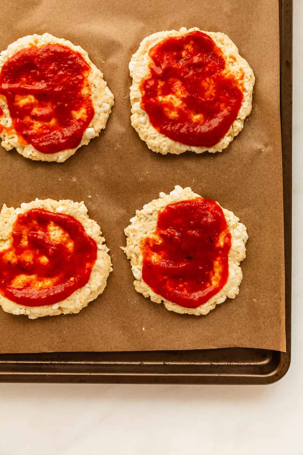 cottage cheese buns topped with pizza sauce on a baking sheet.