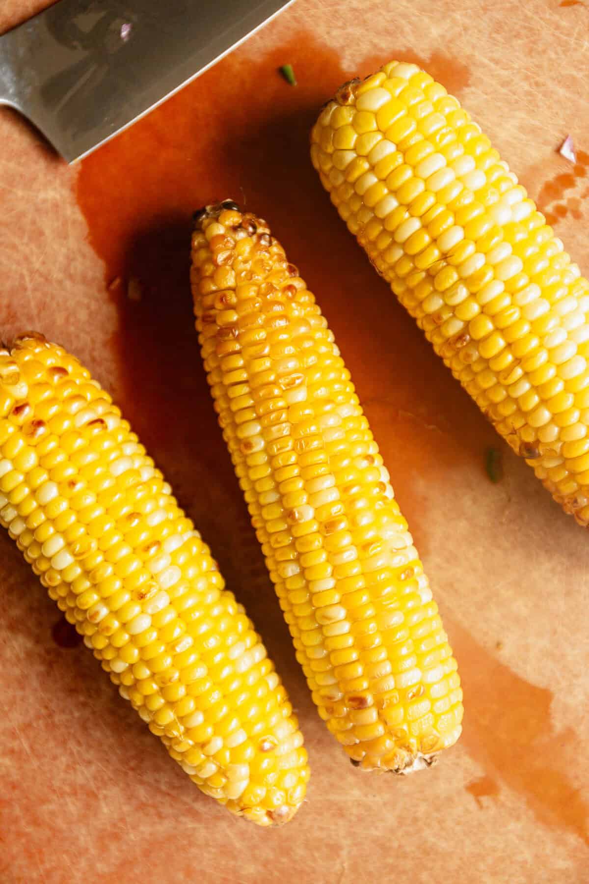 three ears of corn on a wood cutting board.
