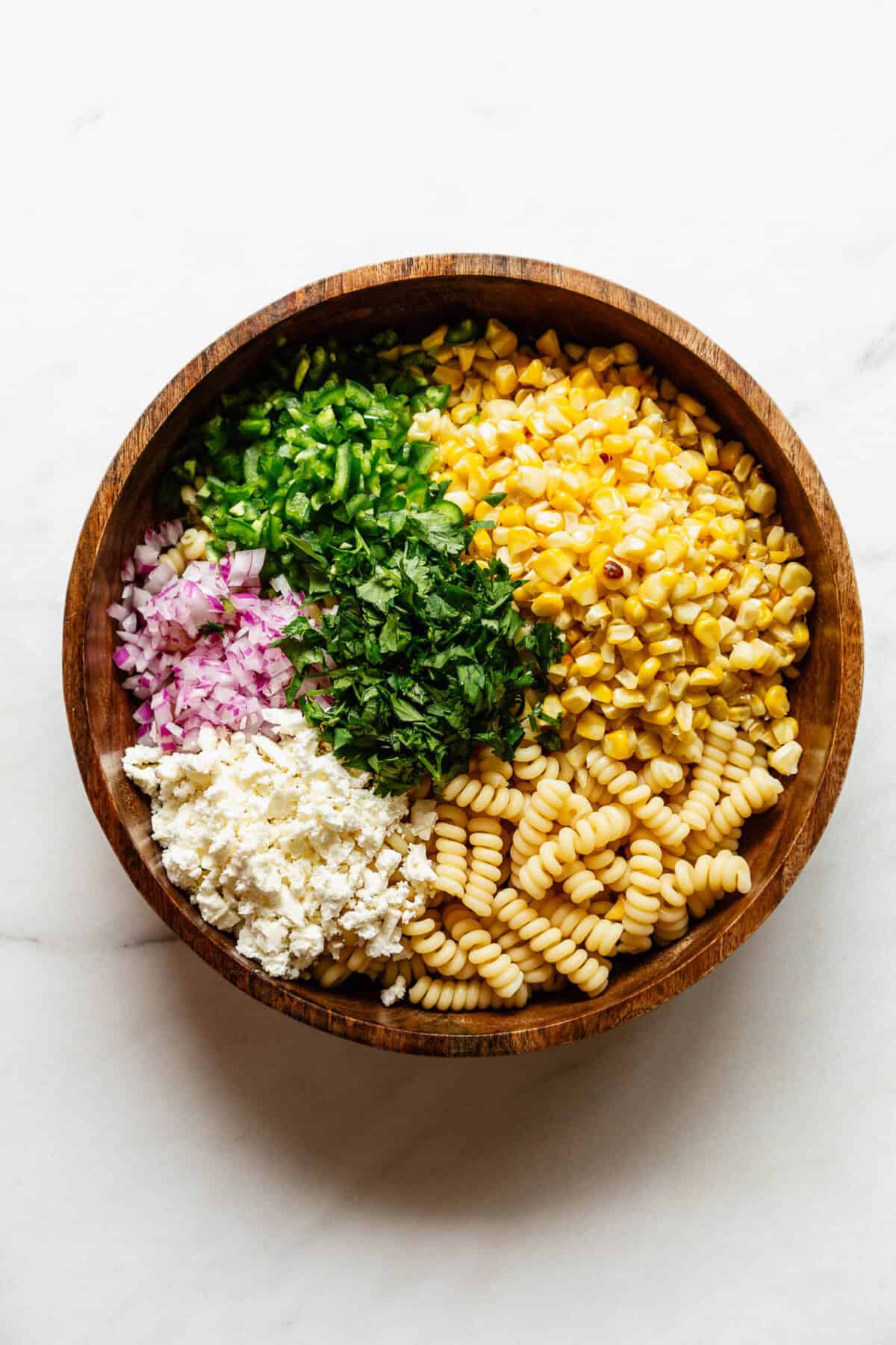 pasta, corn, contija cheese, red onion, jalapeno and cilantro in a wood bowl.