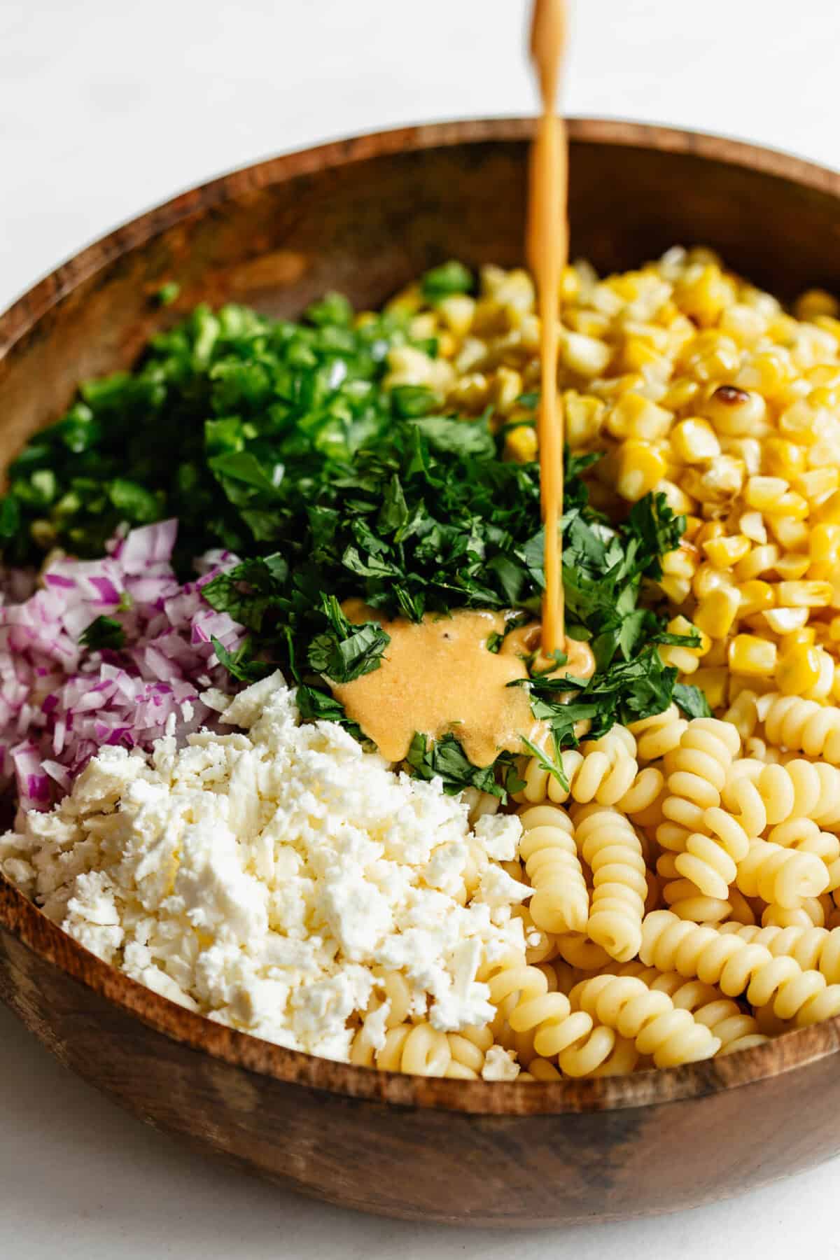 dressing being poured into a bowl of elote pasta salad.