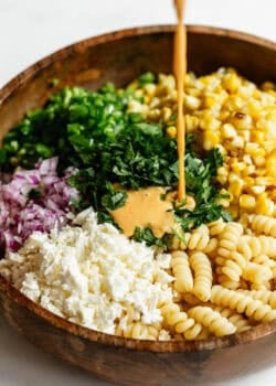 dressing being poured into a bowl of elote pasta salad.