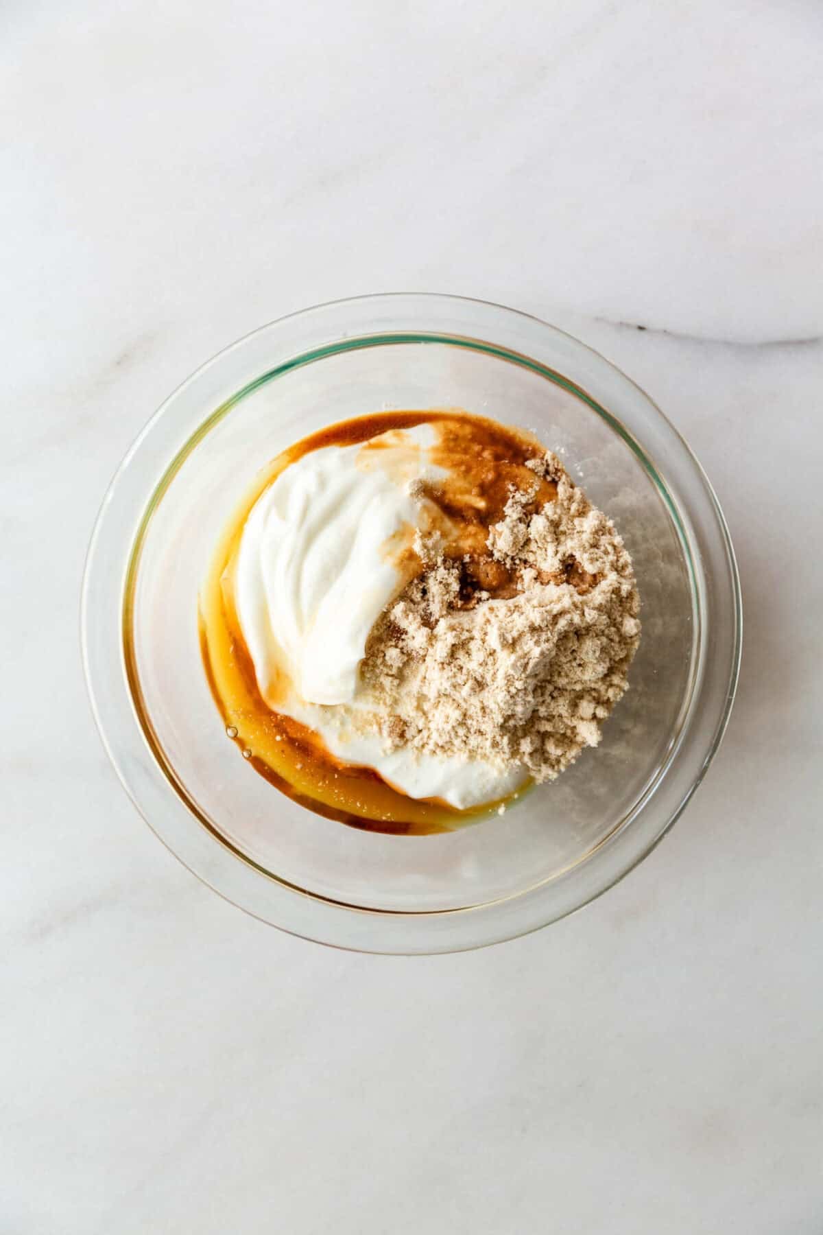 Greek yogurt, protein powder and maple syrup in a clear bowl.