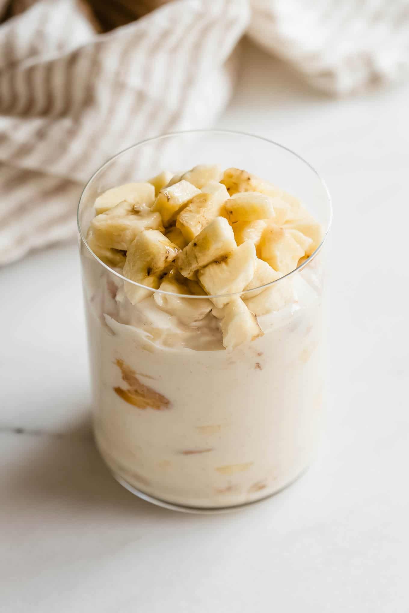 Tall glass jar of high protein banana pudding topped with banana slices.
