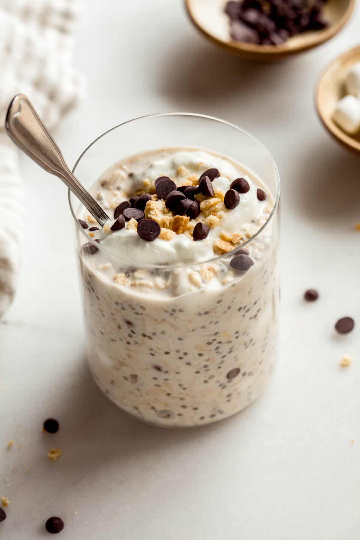 A jar of smores overnight oats topped with graham cracker crumbs and chocolate chips with a spoon in it.