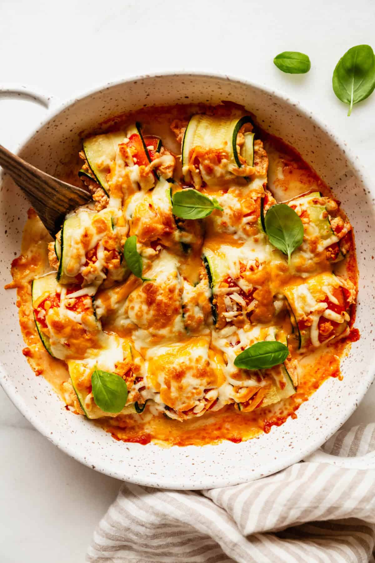 Buffalo chicken zucchini roll ups topped with basil with a wood spoon.