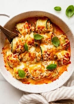 Buffalo chicken zucchini roll ups topped with basil with a wood spoon.