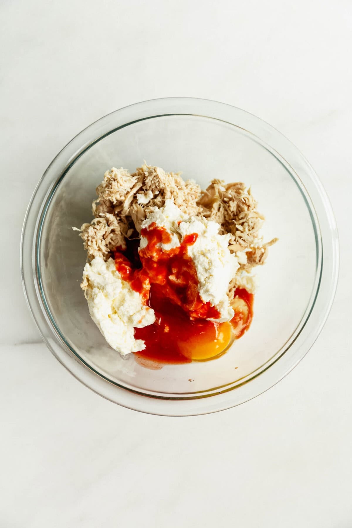 shredded chicken, egg, hot sauce and ricotta in a clear mixing bowl.