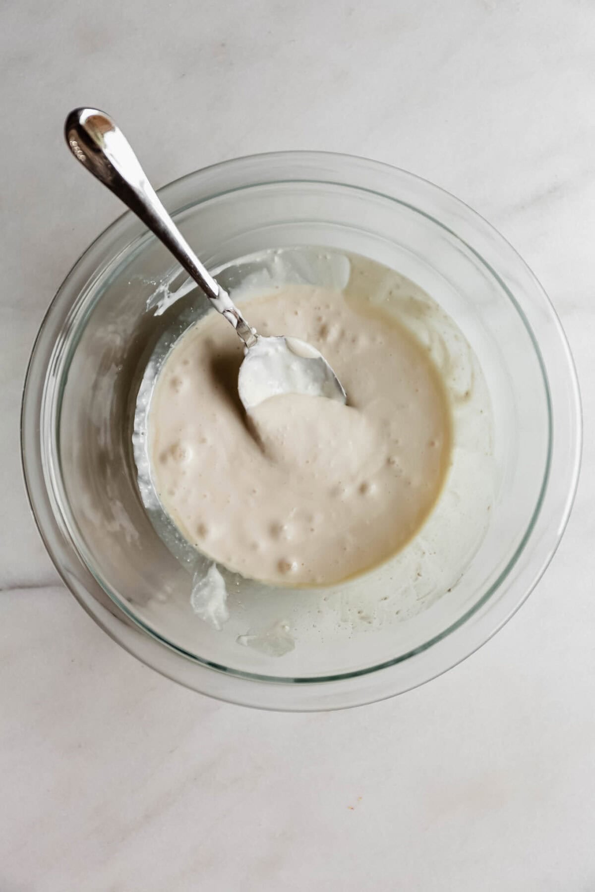 blended cottage cheese with a spoon in a clear mixing bowl.