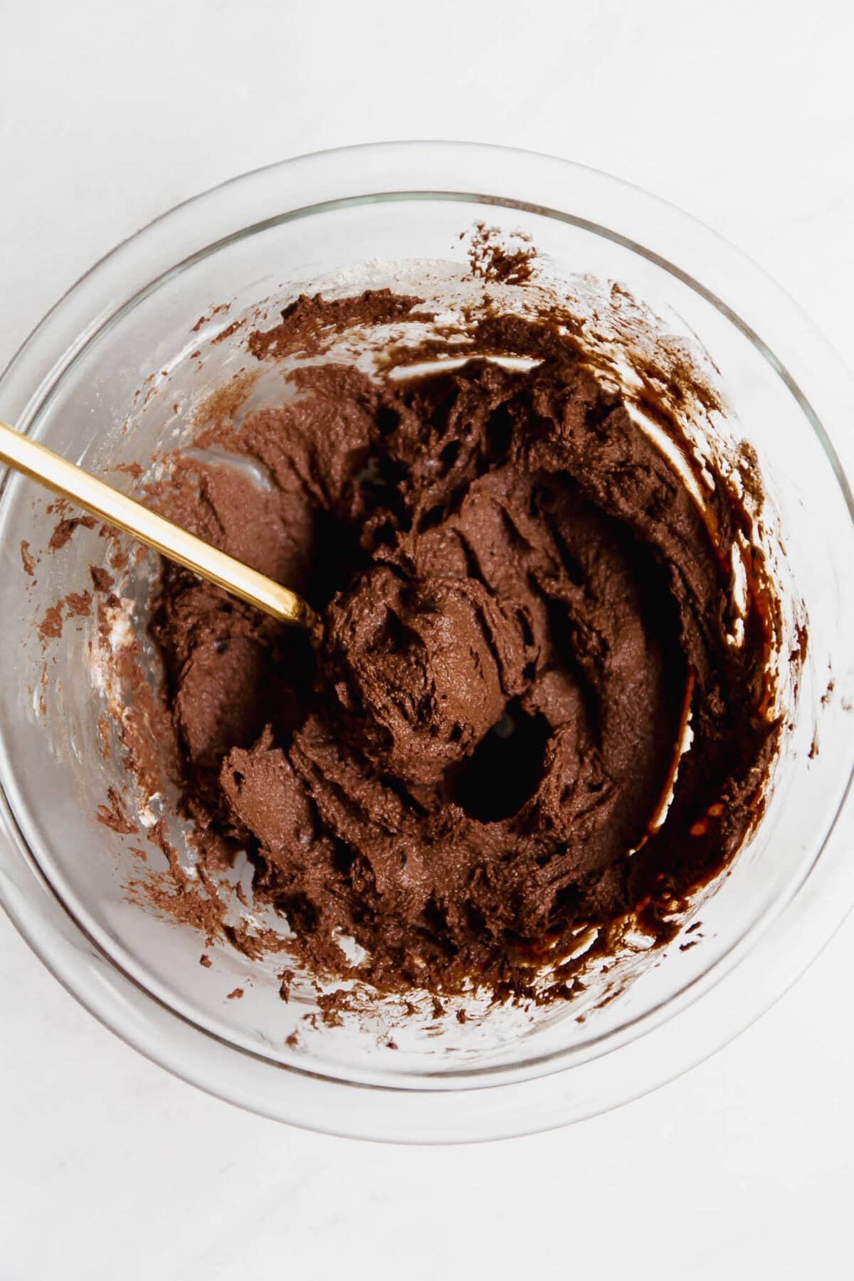 Cottage cheese brownie batter in a clear mixing bowl with a gold spoon.
