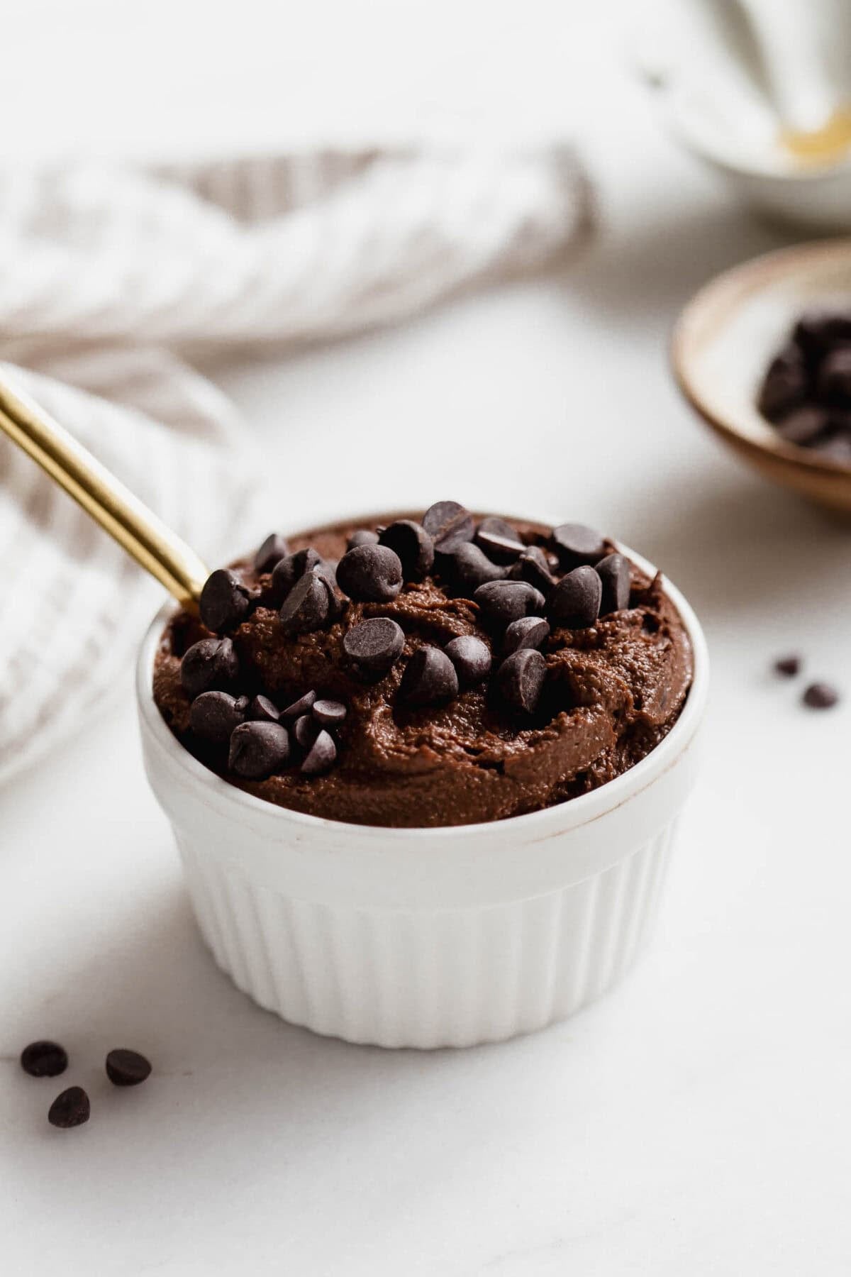 Cottage cheese brownie batter in a white ramekin with a gold spoon with a napkin on the side.