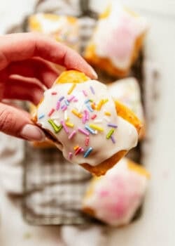 a hand holding a Cottage cheese dough pop tart topped with icing and rainbow sprinkles.
