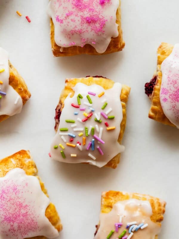 Cottage cheese dough pop tarts topped with icing sugar and sprinkles on a marble counter.