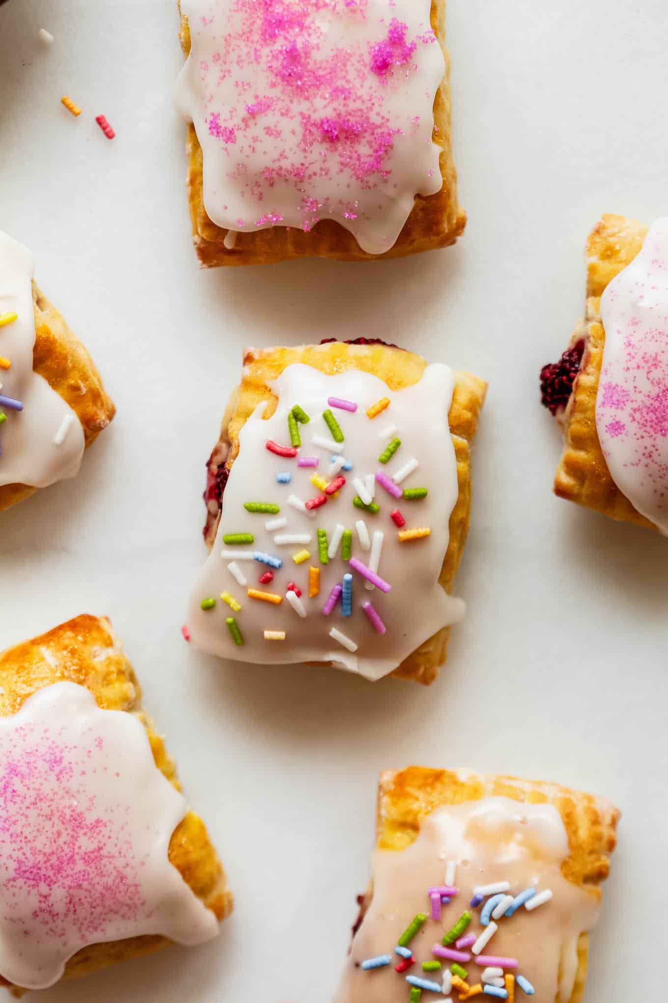 Cottage cheese dough pop tarts topped with icing sugar and sprinkles on a marble counter.