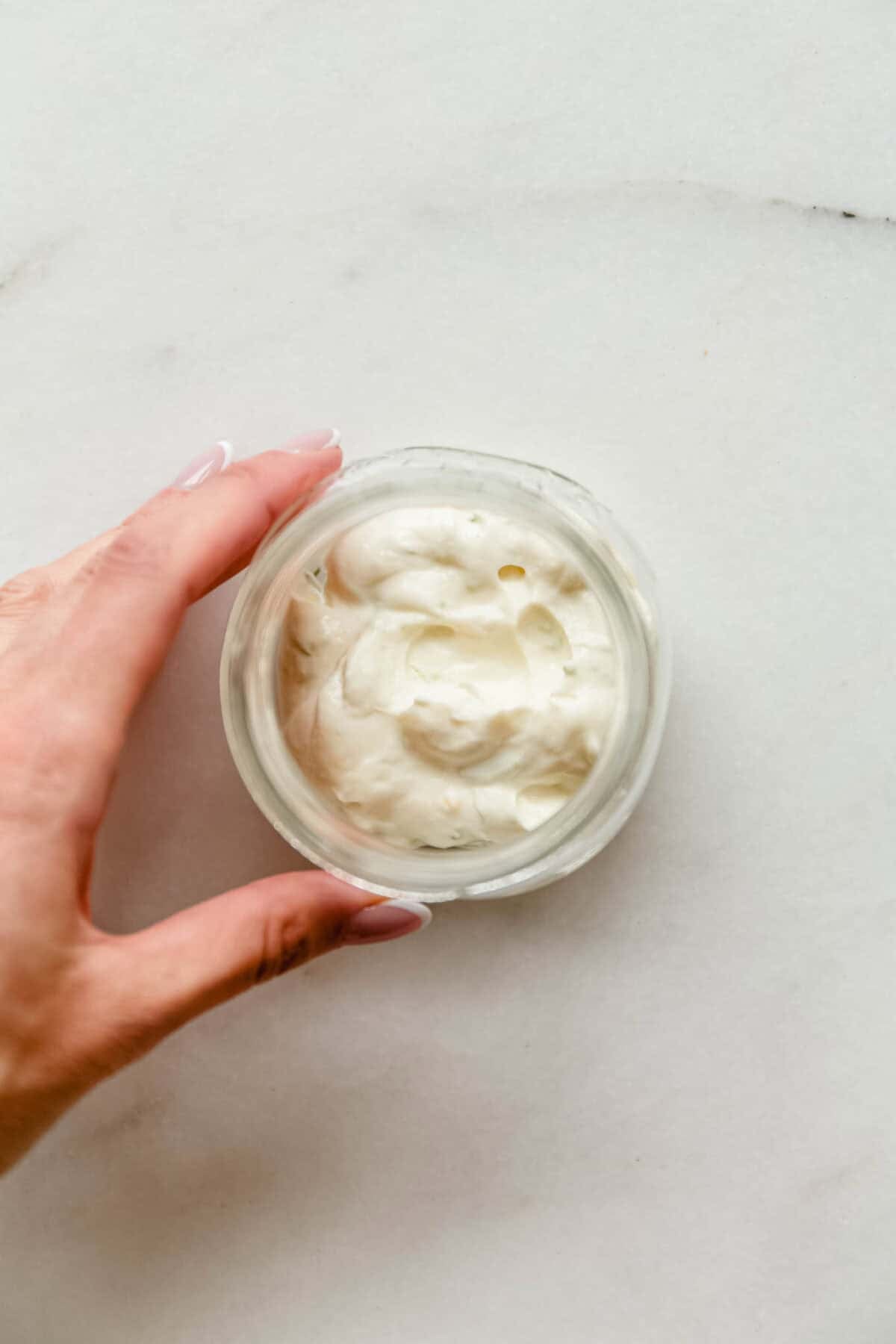 Hand holding a glass jar of creamy key lime pie filling made with Greek yogurt.