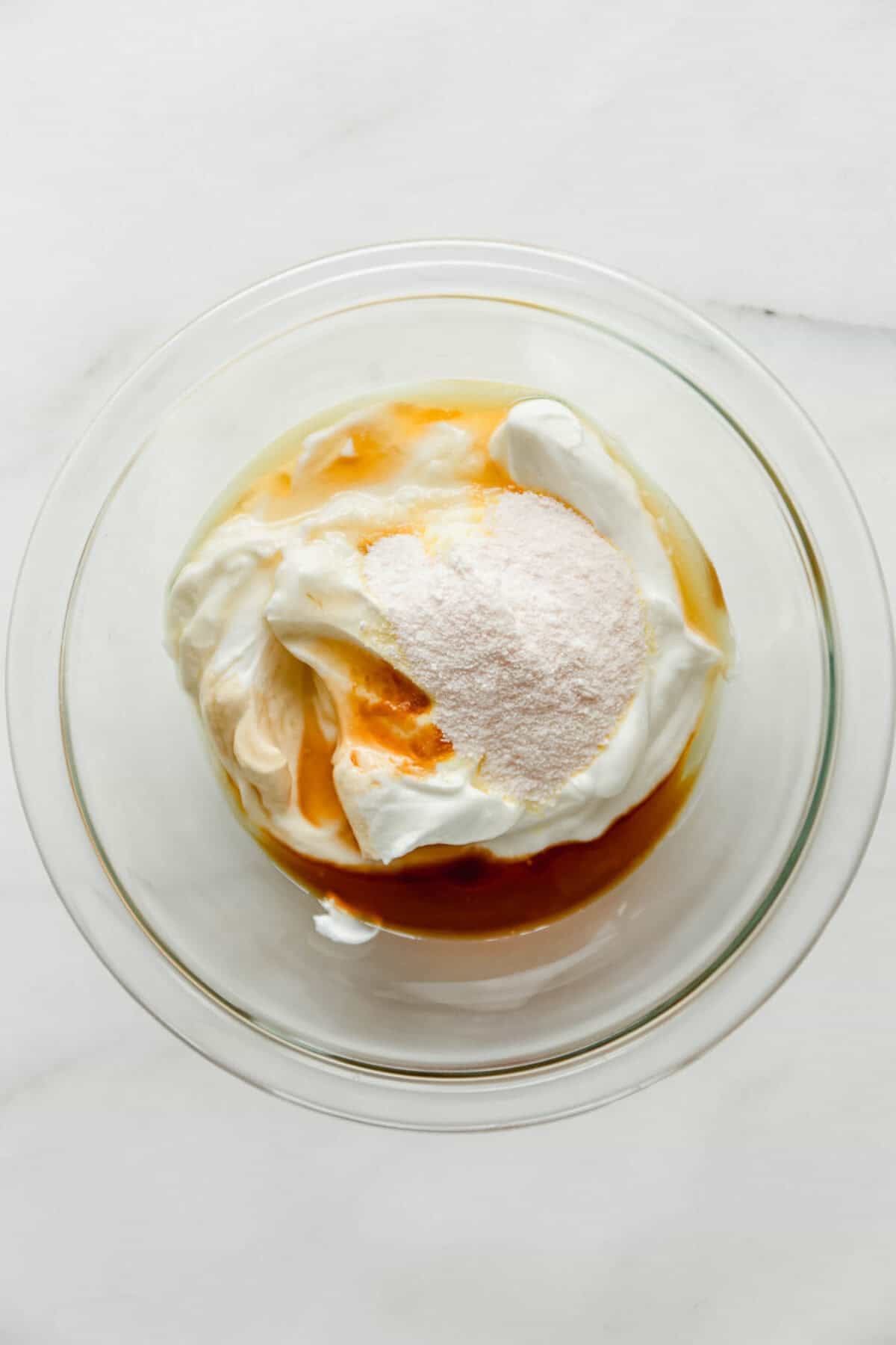 Greek yogurt, vanilla pudding mix and maple syrup in a clear mixing bowl.