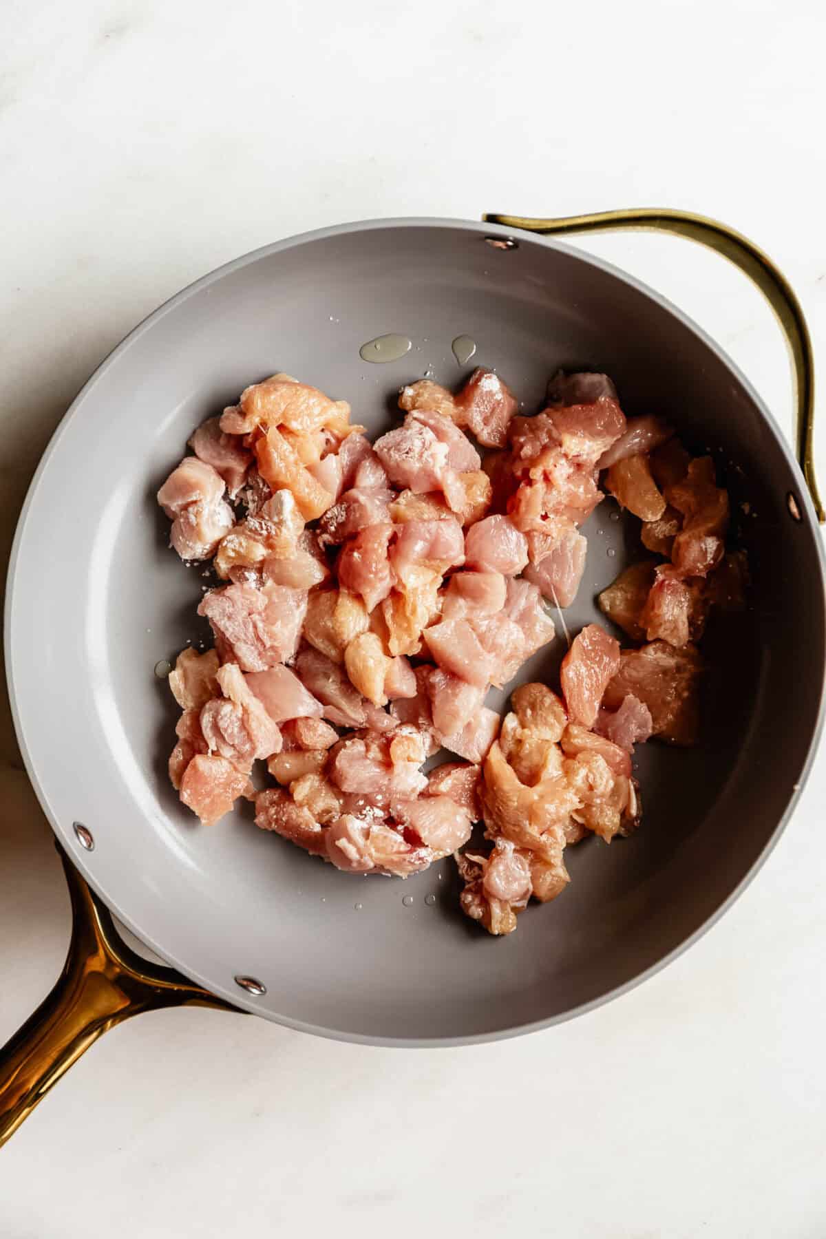 Raw diced chicken breast pieces in a skillet ready to be cooked.