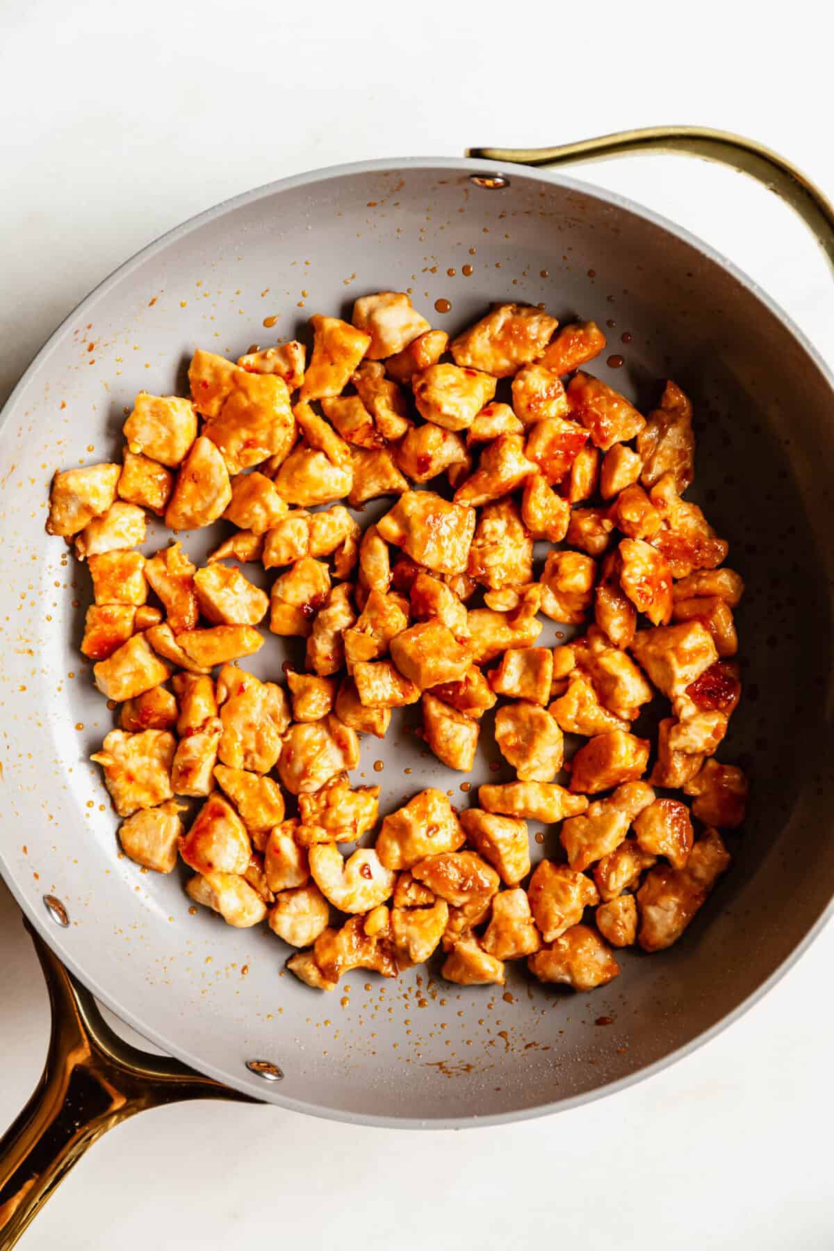 Golden brown chicken bites fully coated in bang bang sauce cooking in a skillet.