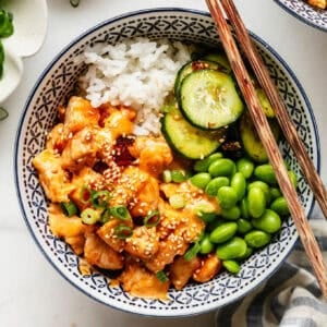 Overhead view of a bang bang chicken rice bowl garnished with sesame seeds and green onion, with a small dish of sesame seeds nearby.