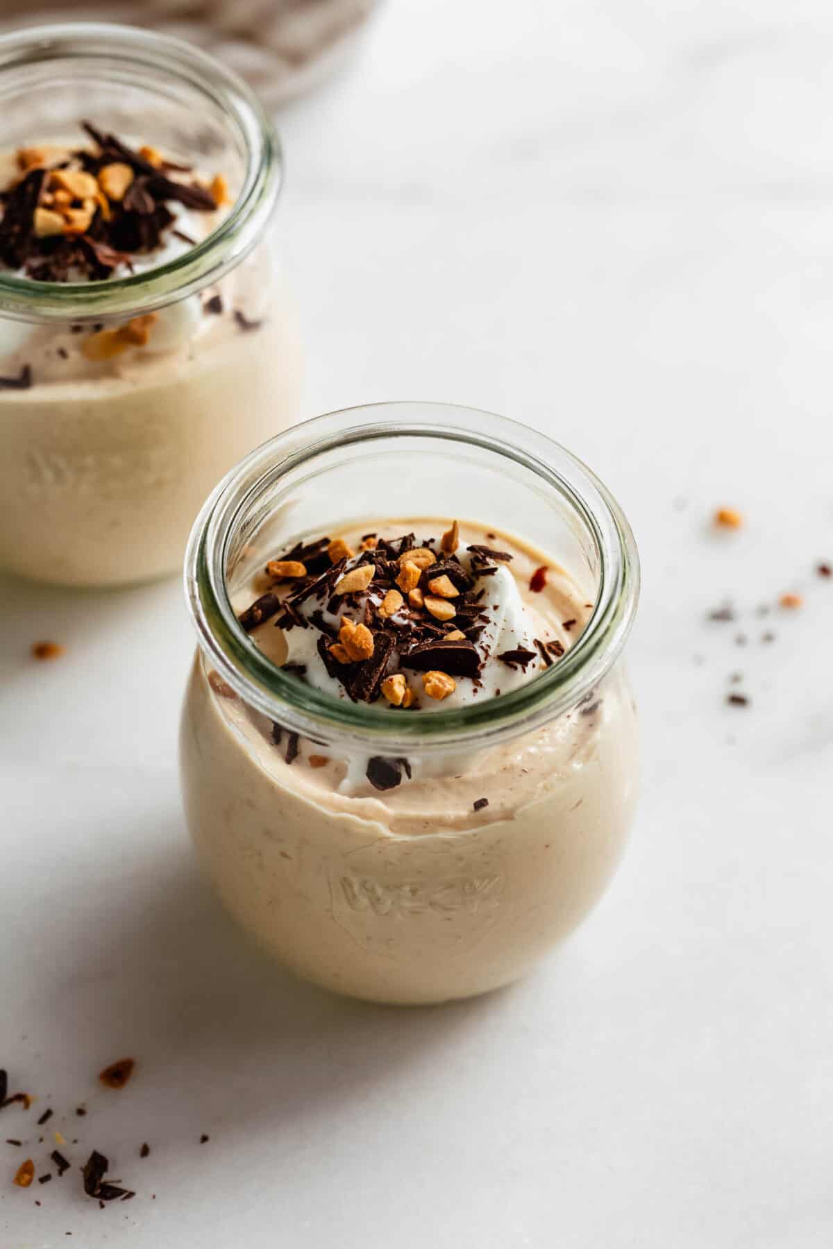 Close-up of a jar of Greek yogurt peanut butter mousse garnished with chopped nuts and chocolate shavings.