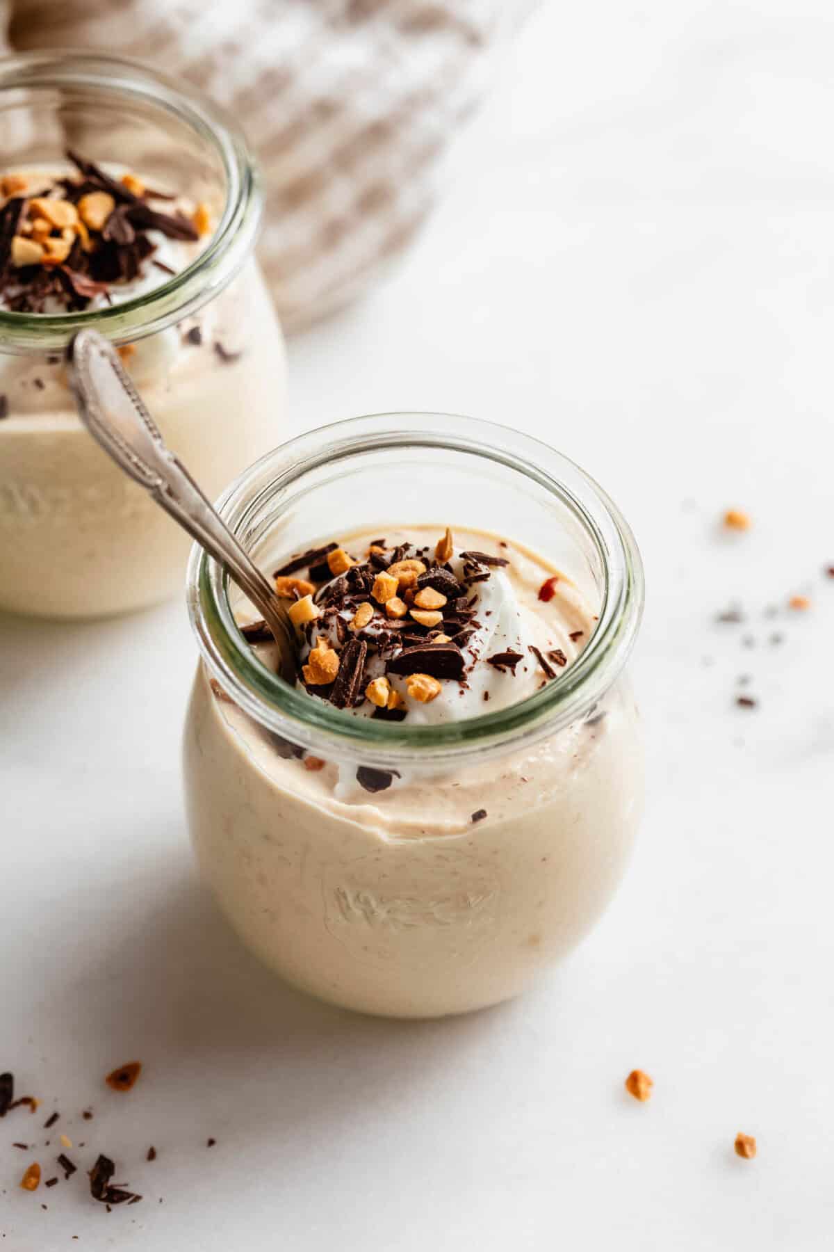 Jar of Greek yogurt peanut butter mousse with a spoon inside, topped with nuts and chocolate shavings.