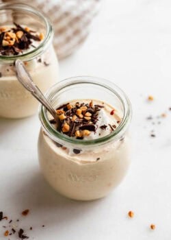 Jar of Greek yogurt peanut butter mousse with a spoon inside, topped with nuts and chocolate shavings.