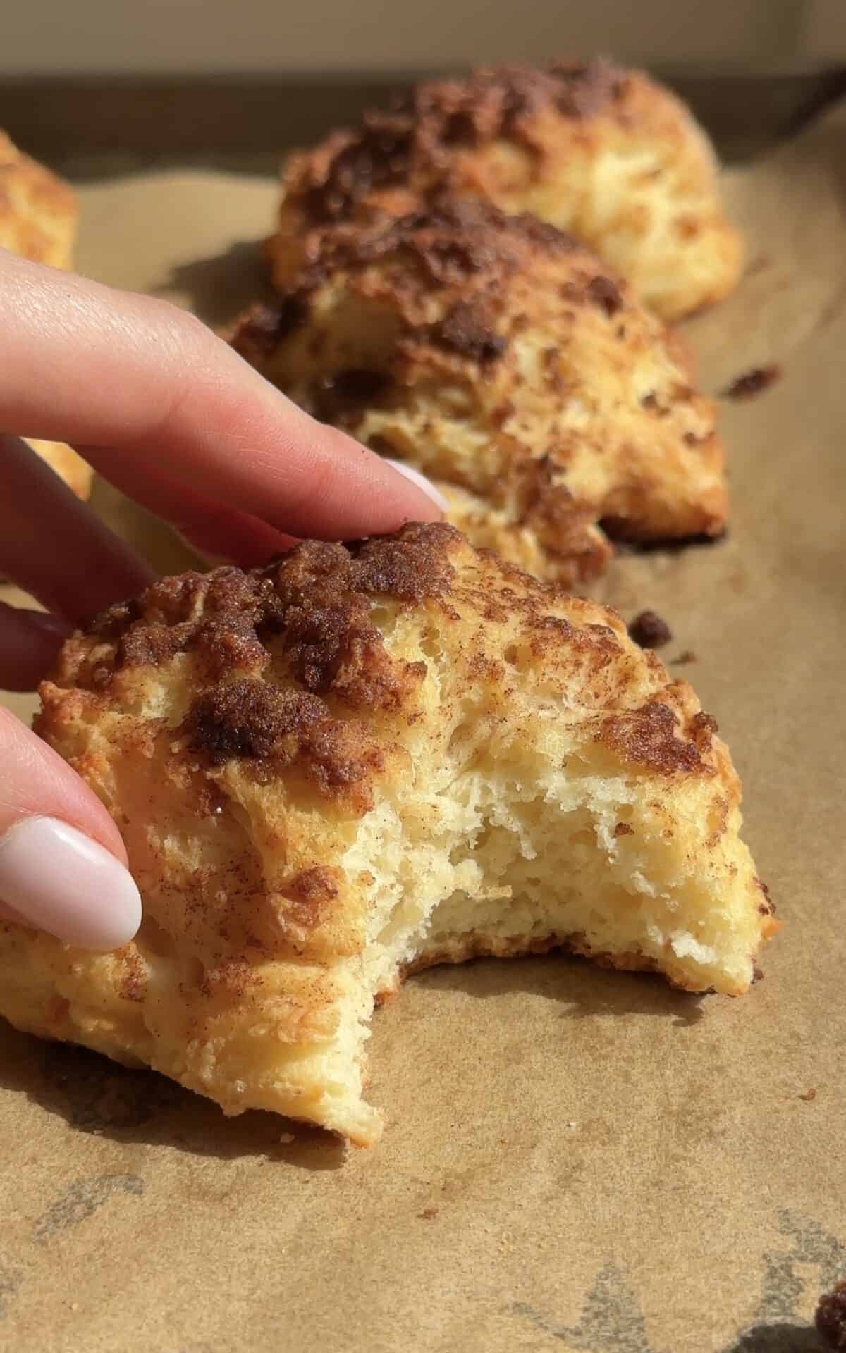 A close up of a hand holding a cottage cheese cinnamon crunch biscuit.