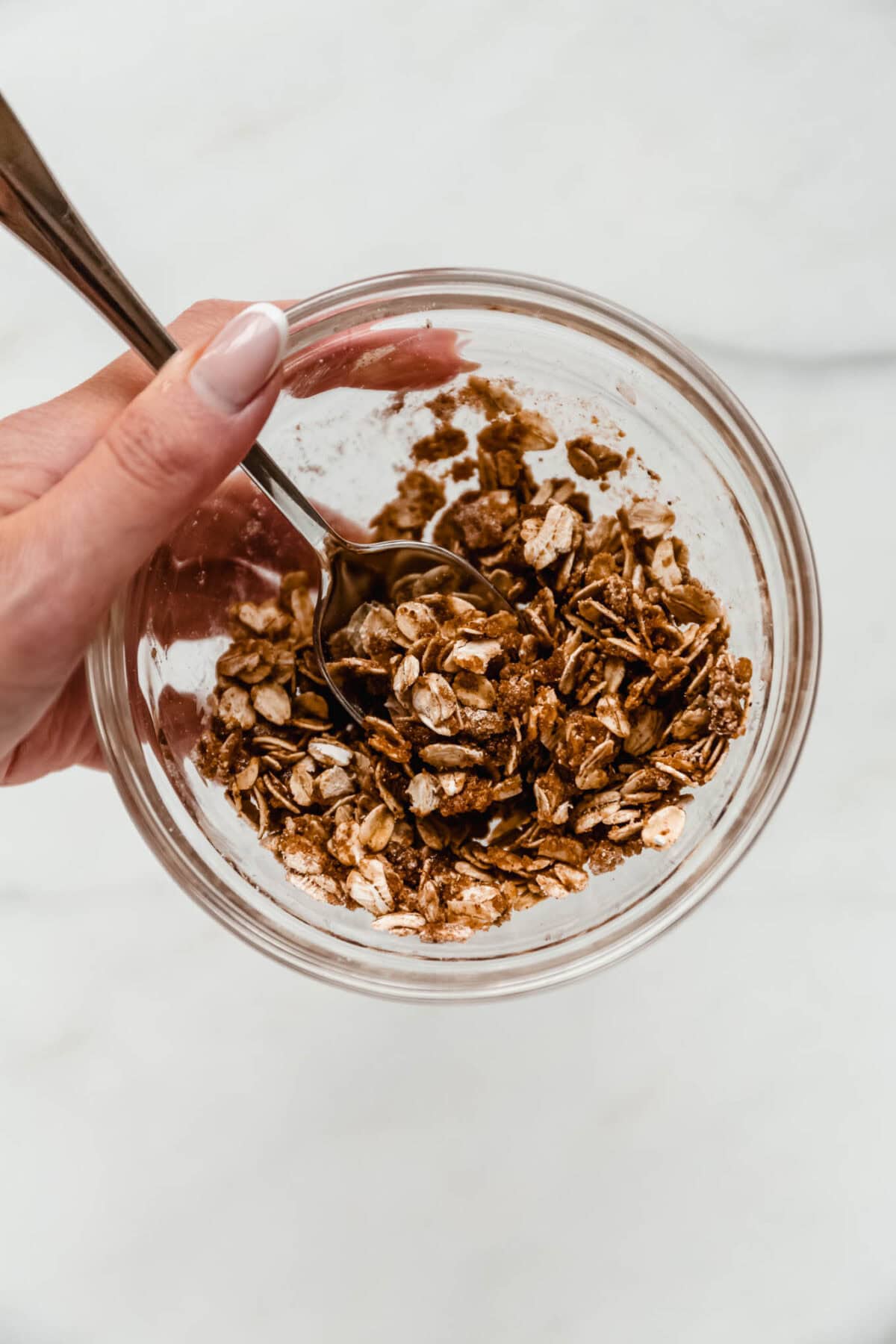 A hand mixing the oat and cinnamon crisp topping in a glass bowl.