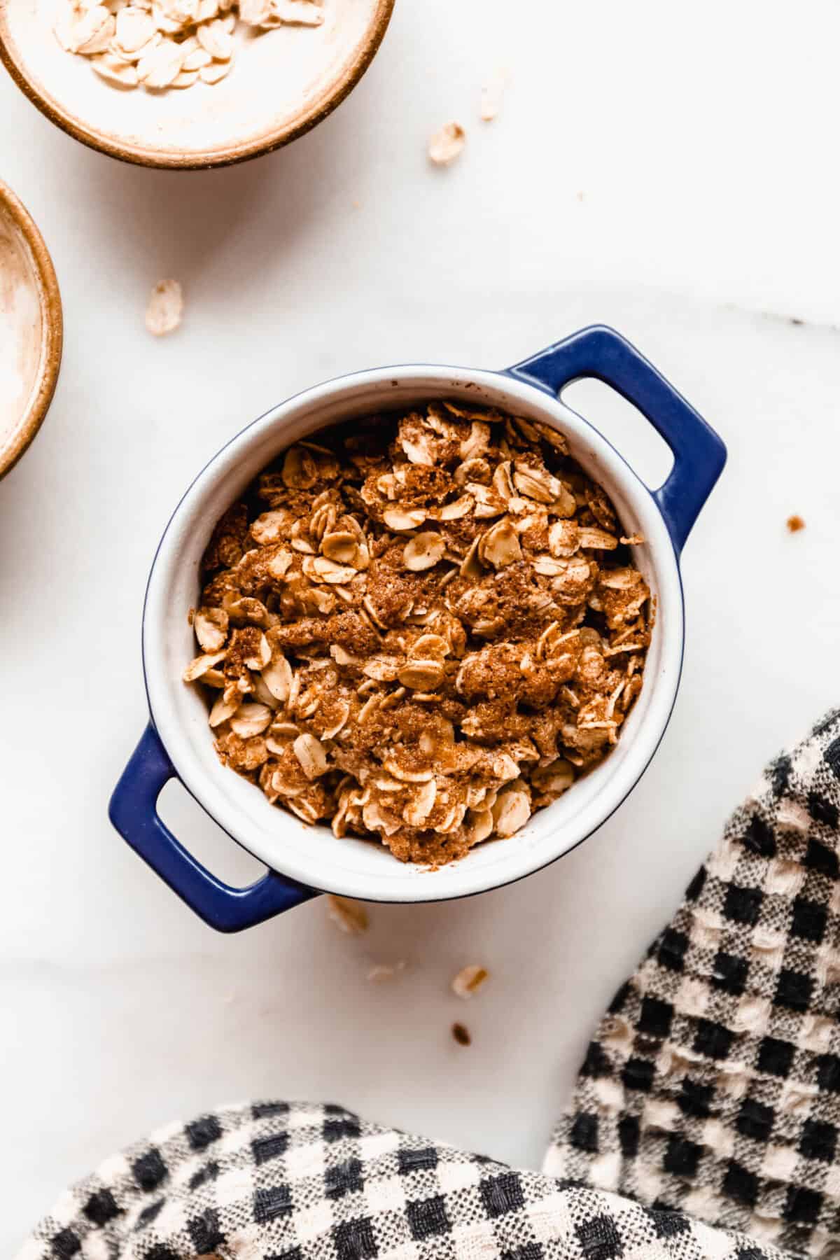 Close-up of the assembled apple crisp with golden oat topping in a small blue dish before baking.